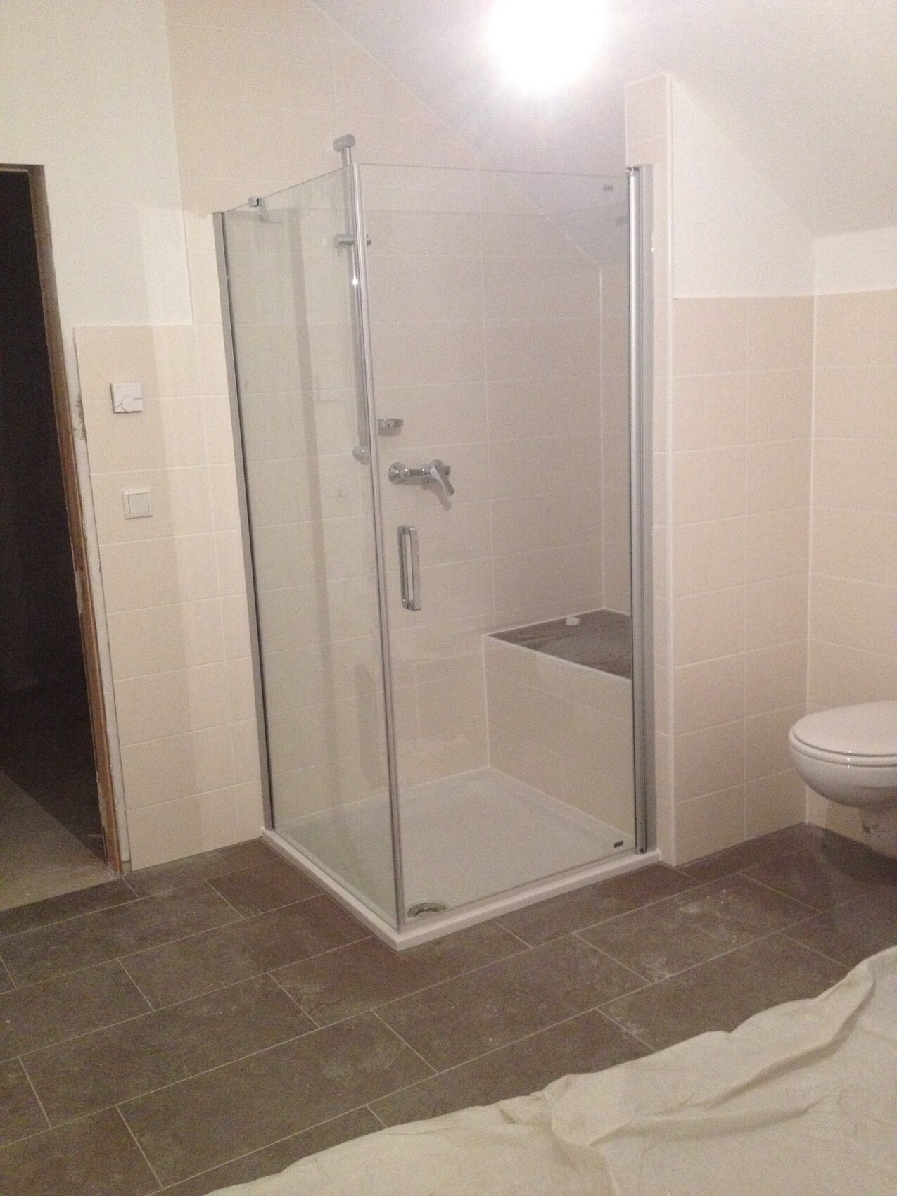 Glas-Duschkabine in beige gefliestem Badezimmer; WC rechts, Boden mit Schutzfolie.