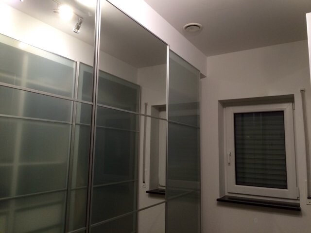 Modernes Badezimmer mit Glas-Schiebetüren, silbernen Profilen und Fenster mit Rollläden.
