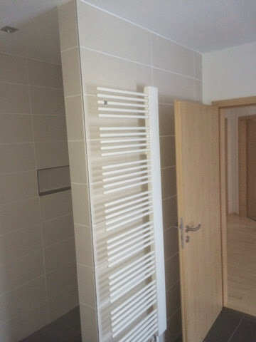Weisser-heizkoerper-im-badezimmer-an-fliesenwand-tuer-offen