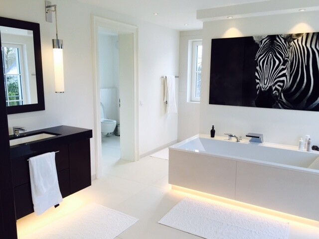 Helles modernes Badezimmer mit eingebetteter Badewanne, schwarzem Waschtisch und Zebra-Wandkunst