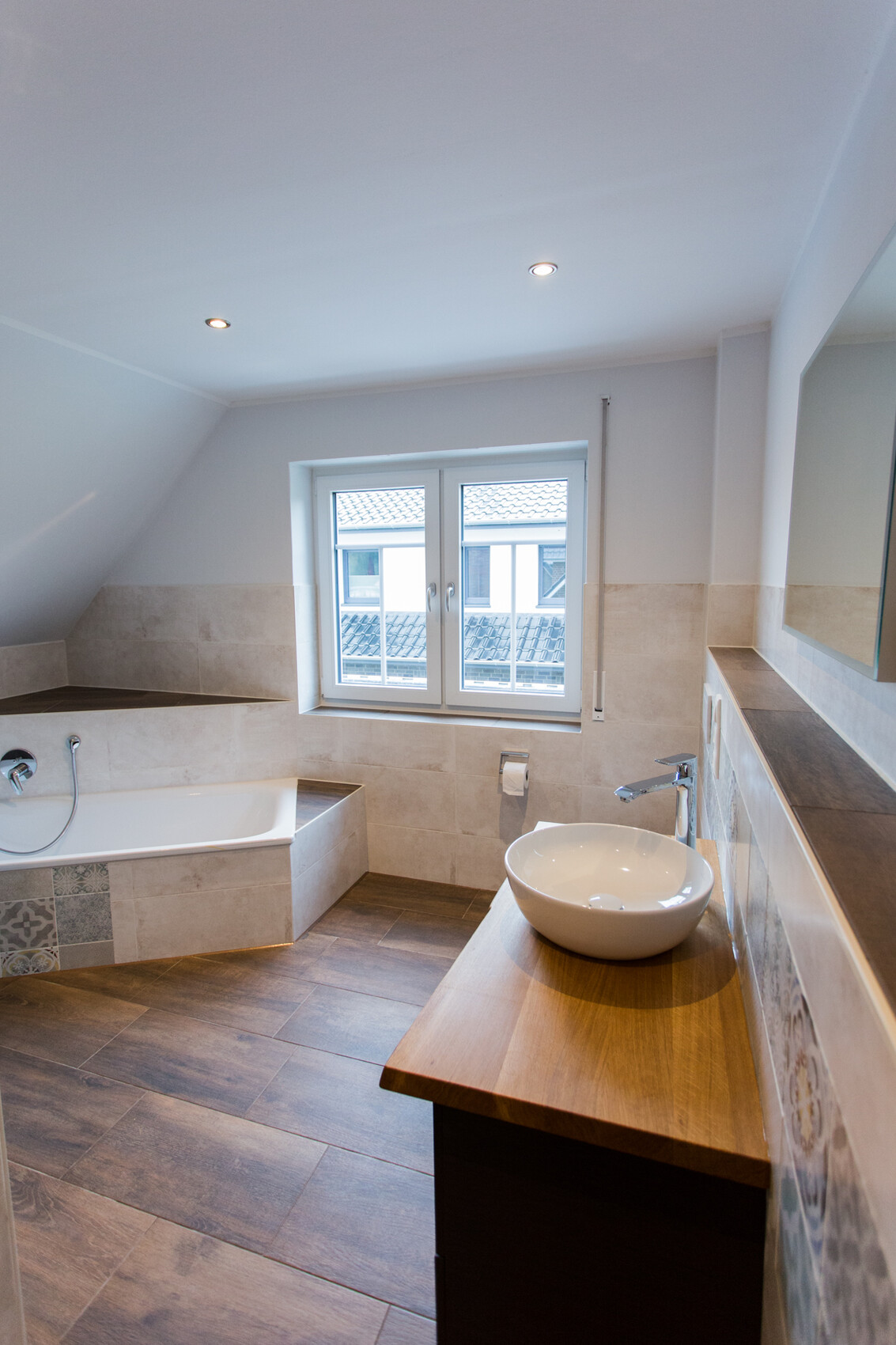 Modernes Badezimmer mit Badewanne, runder Waschbecken auf Holzablage, Fenster und hellen Fliesen