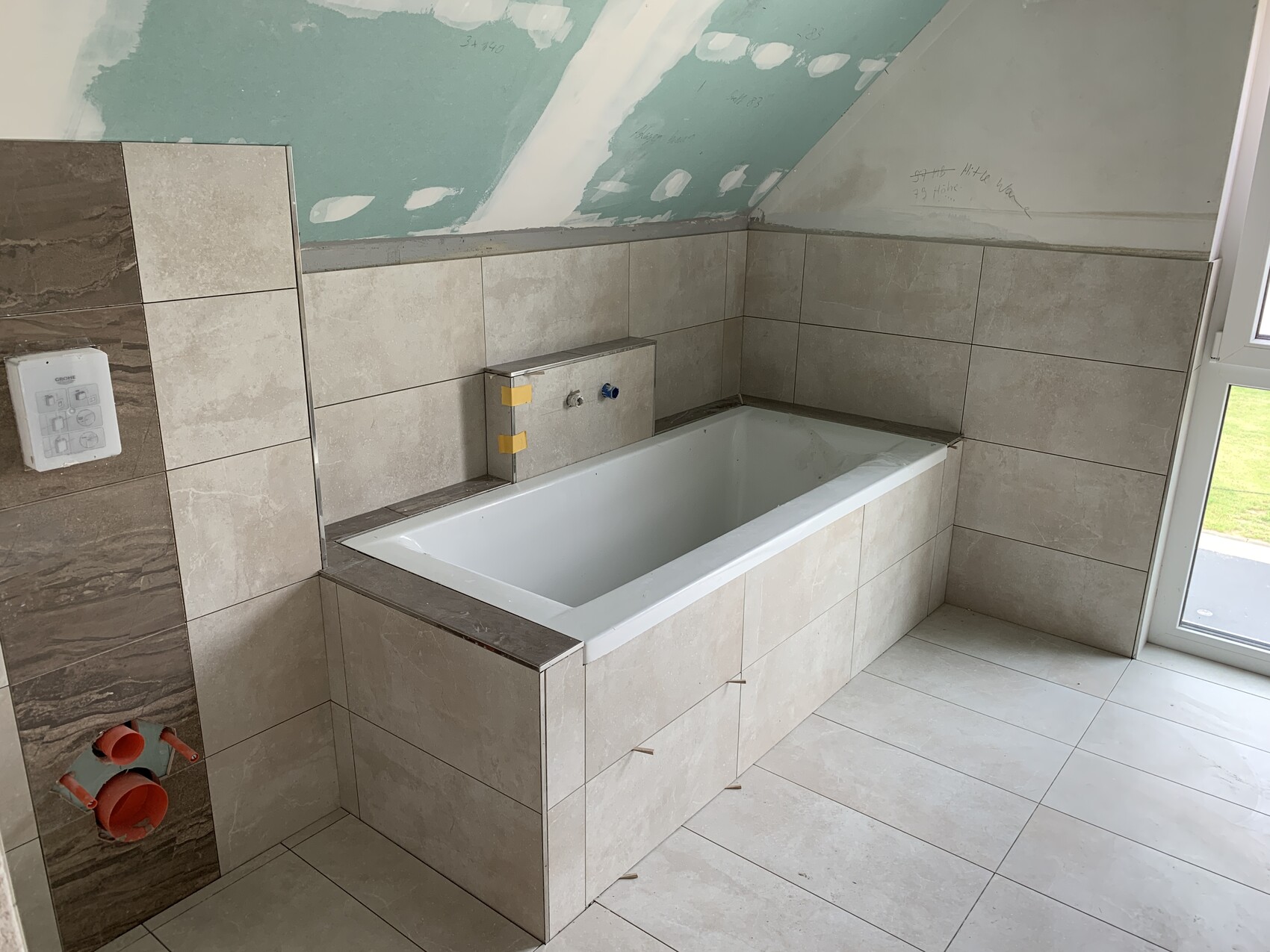 Badezimmer im Bau mit eingebauter Badewanne, beige Fliesen und grün gestrichener Wand.