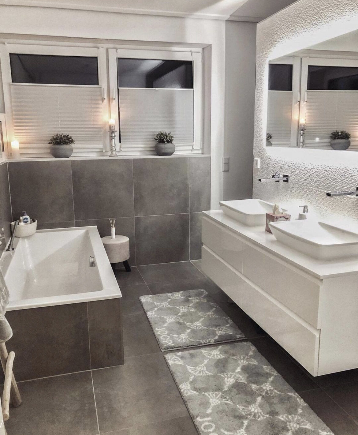 Modernes Badezimmer: Wanne links, Doppelwaschtisch rechts, Kerzen, Pflanzen, graue Fliesen.