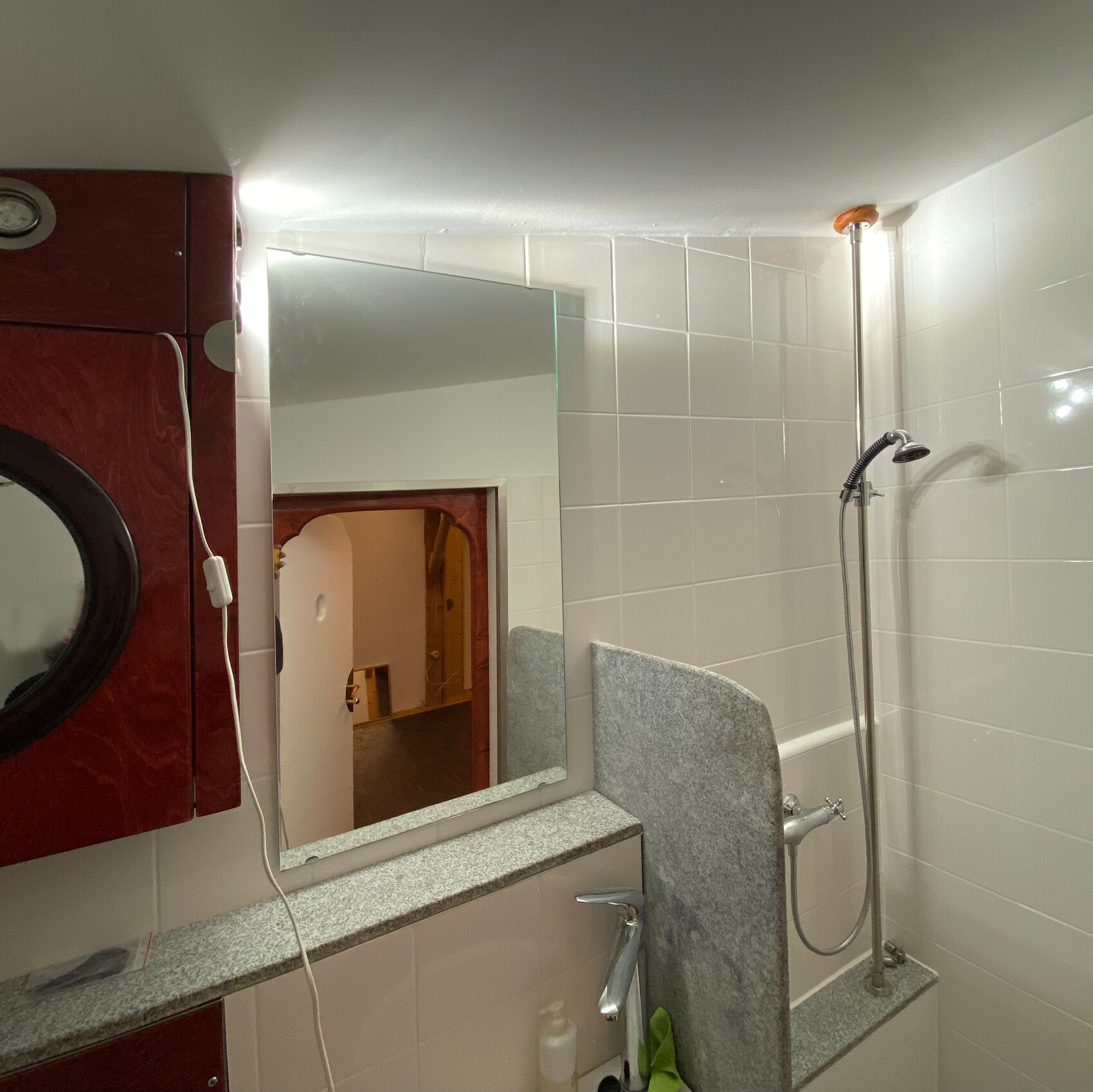 Badezimmer mit Dusche, Spiegel, Waschtisch und weißen Fliesen an den Wänden