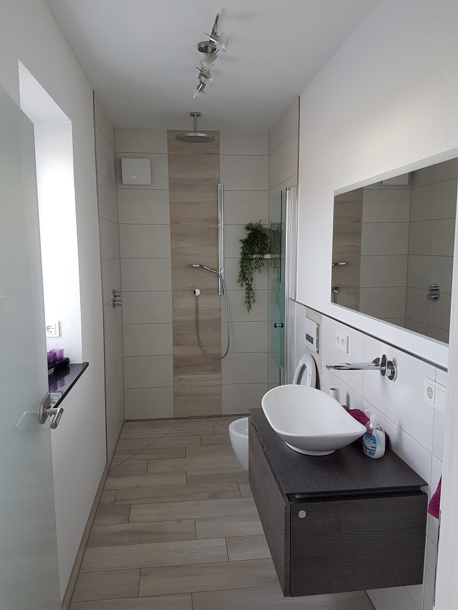 Modernes Badezimmer: Dusche mit Glasabtrennung, Waschtisch aus dunklem Holz und Pflanze.