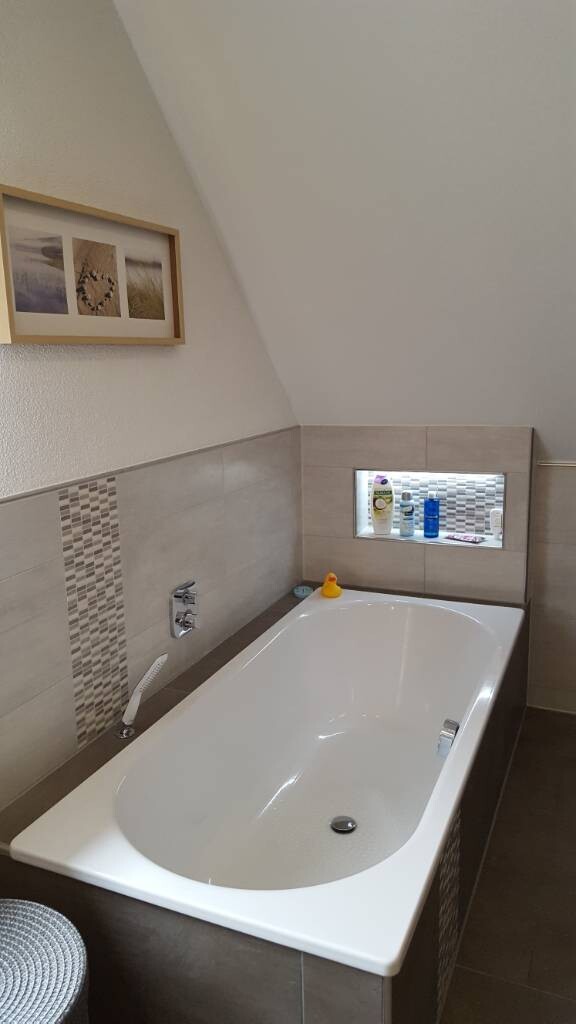 Badezimmer mit eingebauter Badewanne, Wandfliesen, Ablage mit Pflegeprodukten und Wandbild