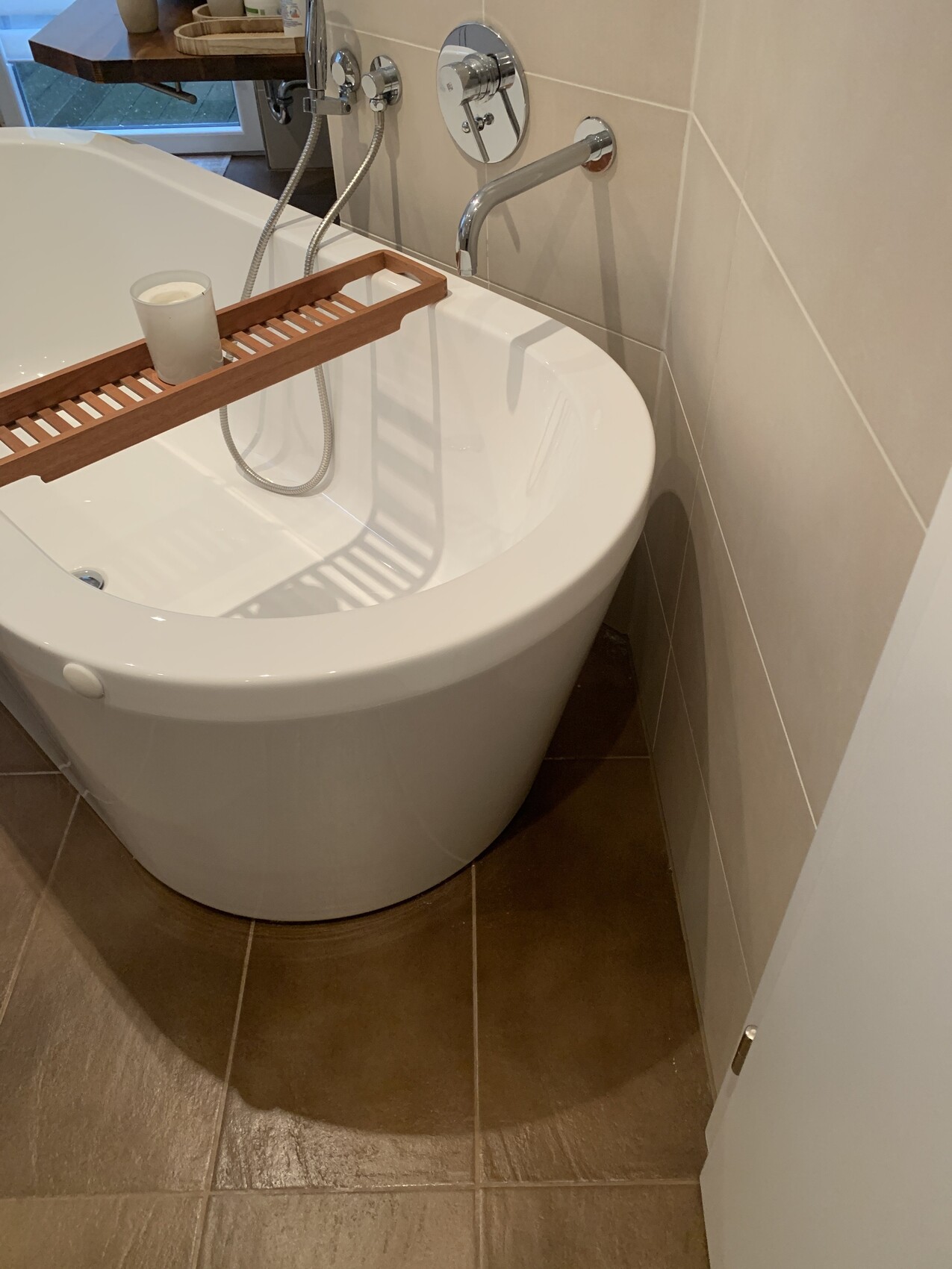 Weiße freistehende Badewanne mit Holzbadewannenbrett und Kerze darauf, Bad mit Fliesen
