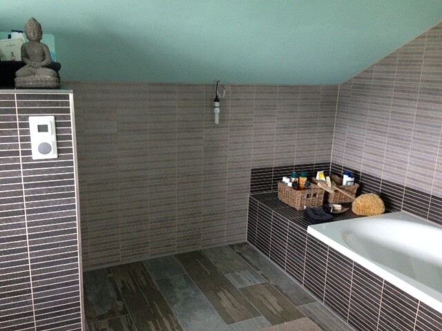 Badezimmer mit grauen Fliesen, Badewanne, Ablagekorb und Badzubehör.
