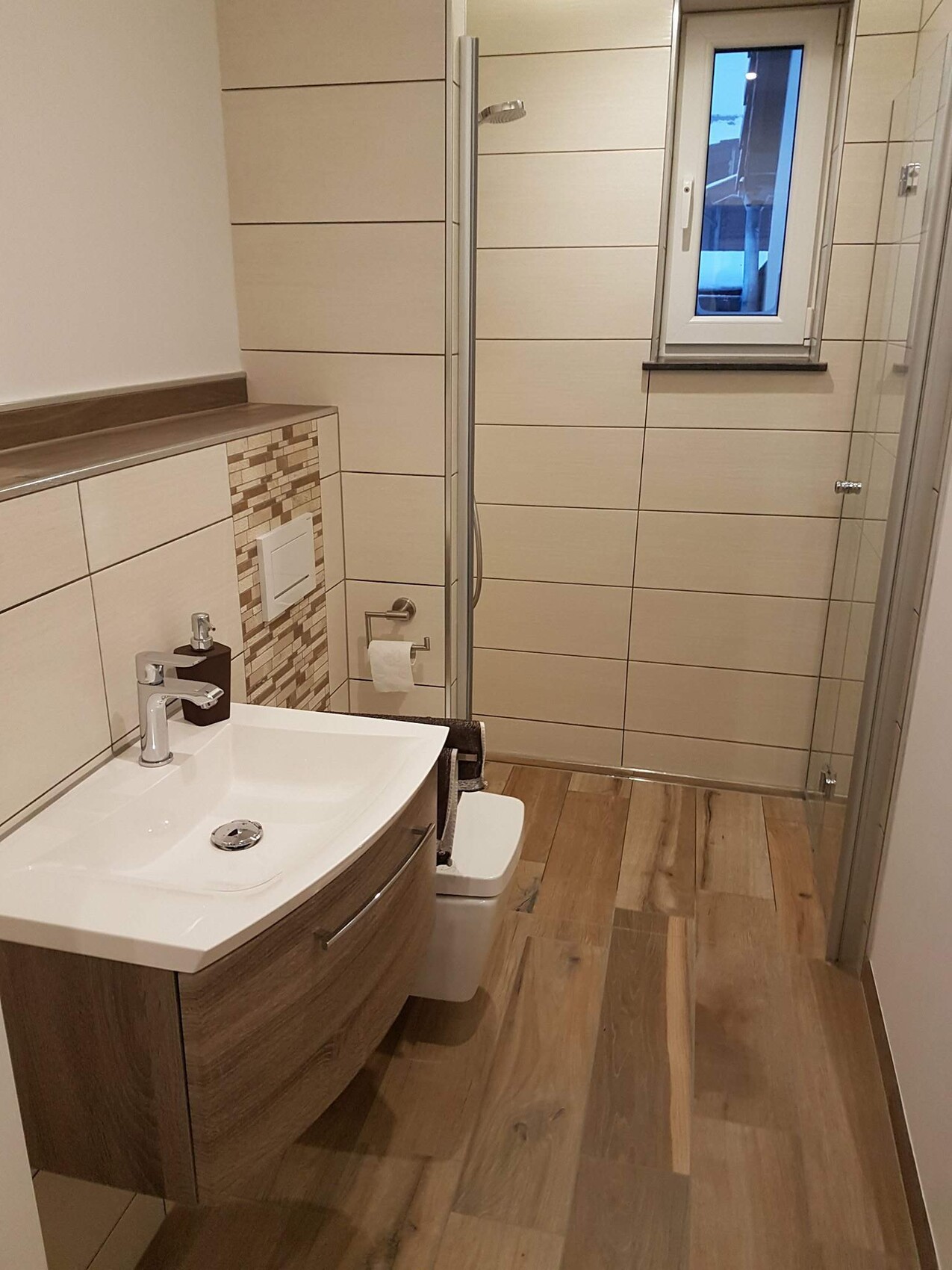 Modernes Badezimmer: Holz-Waschtisch mit weißer Keramik, Glasdusche, WC, Fenster und beige Fliesen.