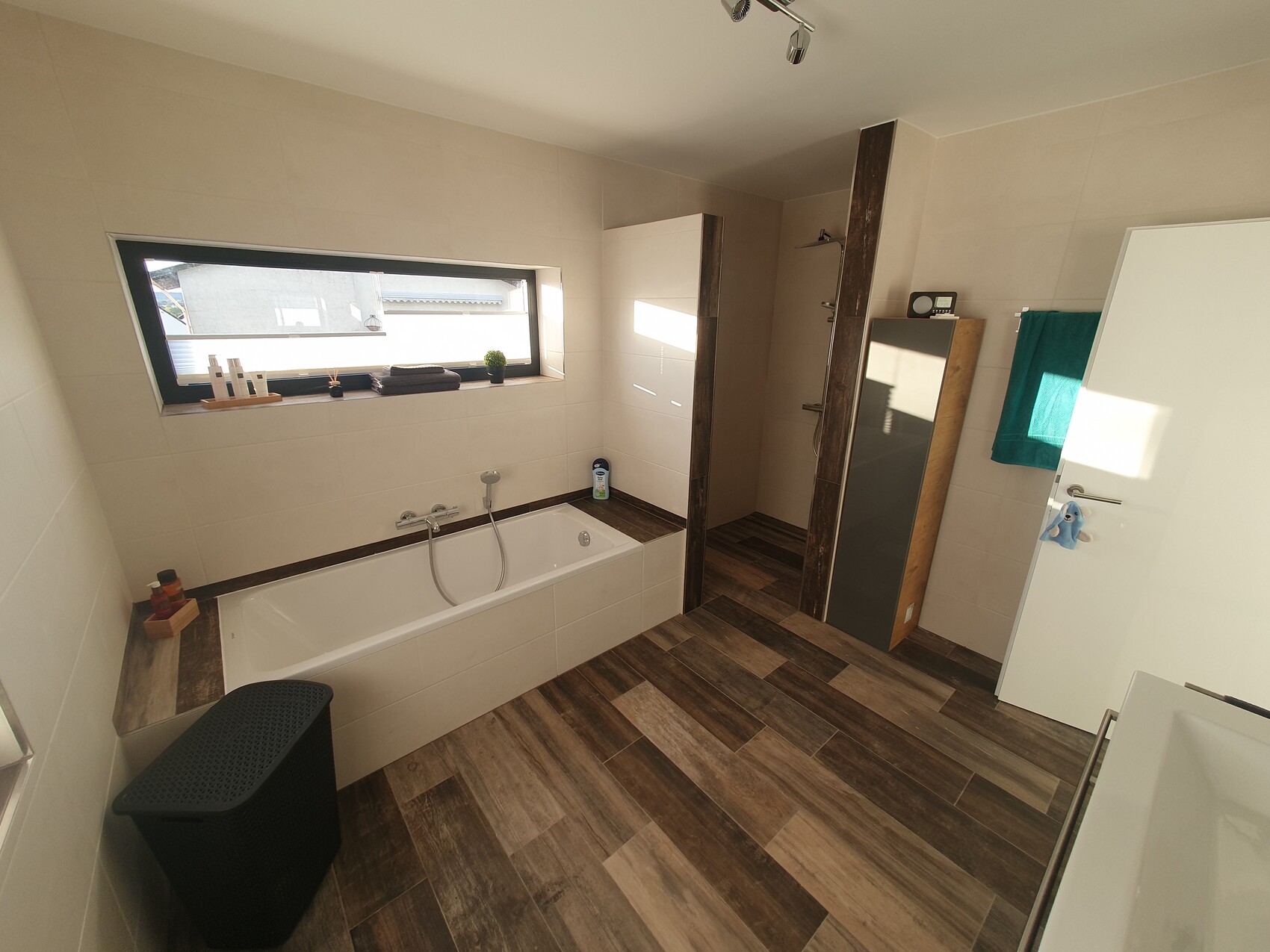 Modernes Badezimmer: Badewanne links, breites Fenster über Wanne, Dusche, Holzoptikboden.
