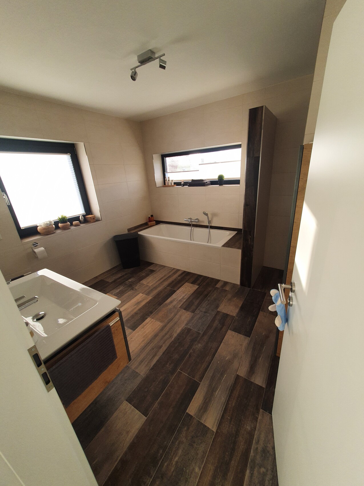 Modernes Badezimmer mit eingebauter Badewanne, Waschbecken, Holzfliesen und Fenster.