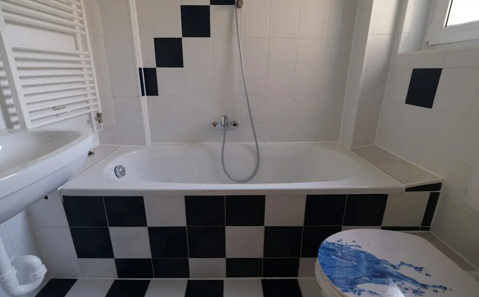 Badezimmer mit Badewanne, Dusche, Waschbecken; schwarz-weiße Fliesen, WC-Sitz mit blauem Muster
