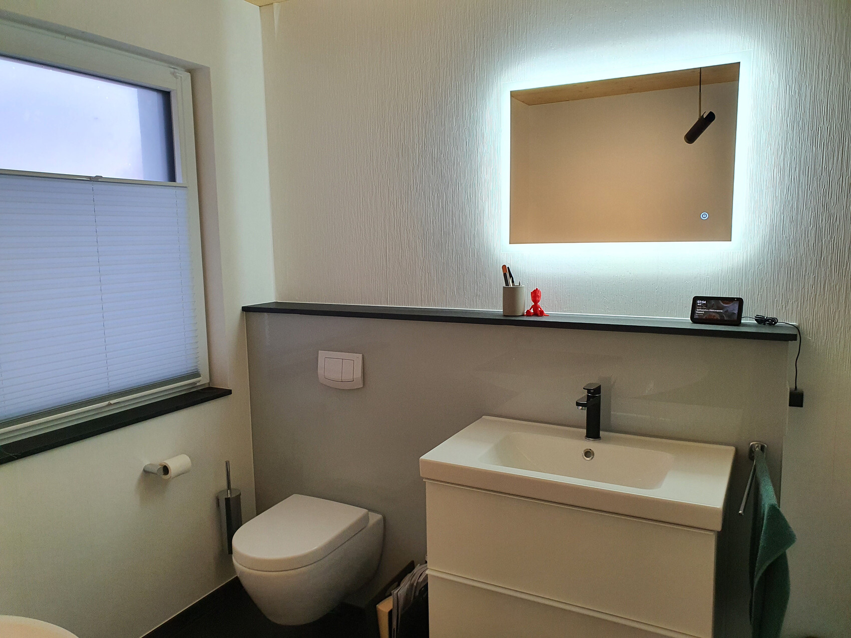 Badezimmer mit Waschbecken, Armatur in Schwarz, beleuchtetem Spiegel, Toilette und Smartphone