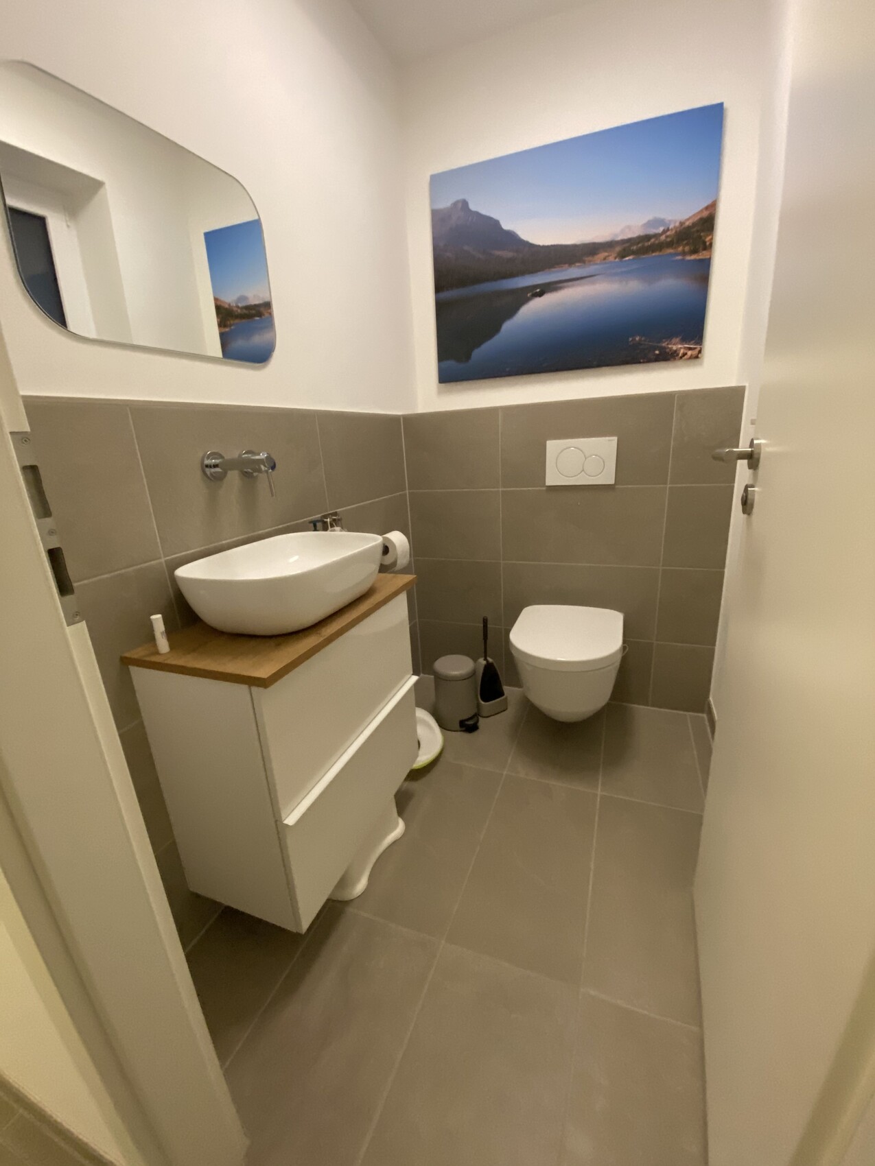 Kleines modernes Bad mit Wandtoilette, Waschbecken auf Holzkonsole und Bergsee-Bild.