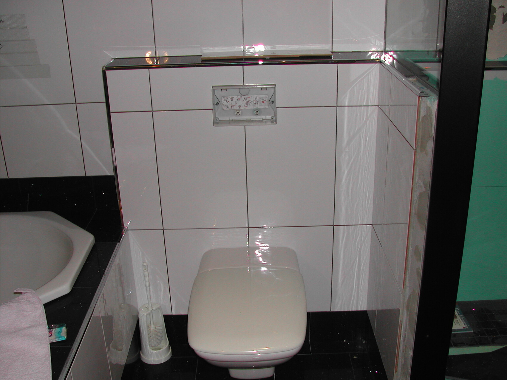 Modernes Badezimmer mit weißer Fliesenwand, Wandtoilette und Spülkasten; links Waschbecken.