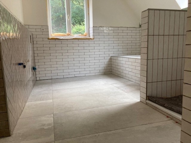 Helles Badezimmer unter Renovierung: weiße Fliesen, Fenster, Badewanne in Nische.