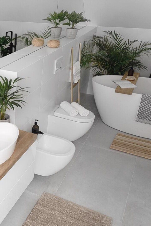 Modernes, helles Badezimmer mit freistehender Badewanne, WC, Pflanzen und Holzdeko.