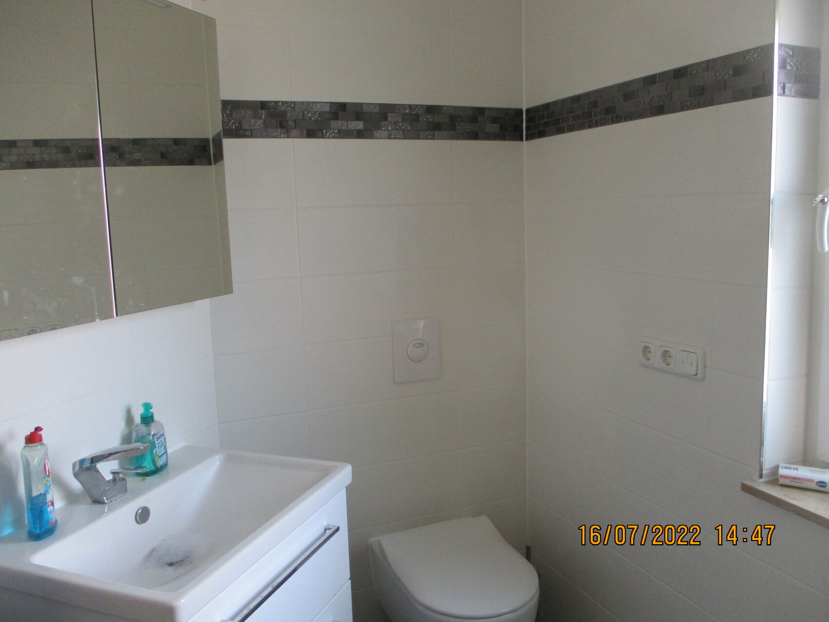 Kleines modernes Badezimmer mit Waschtisch, Armatur, Seifenflaschen, Toilette und Spiegelschrank.