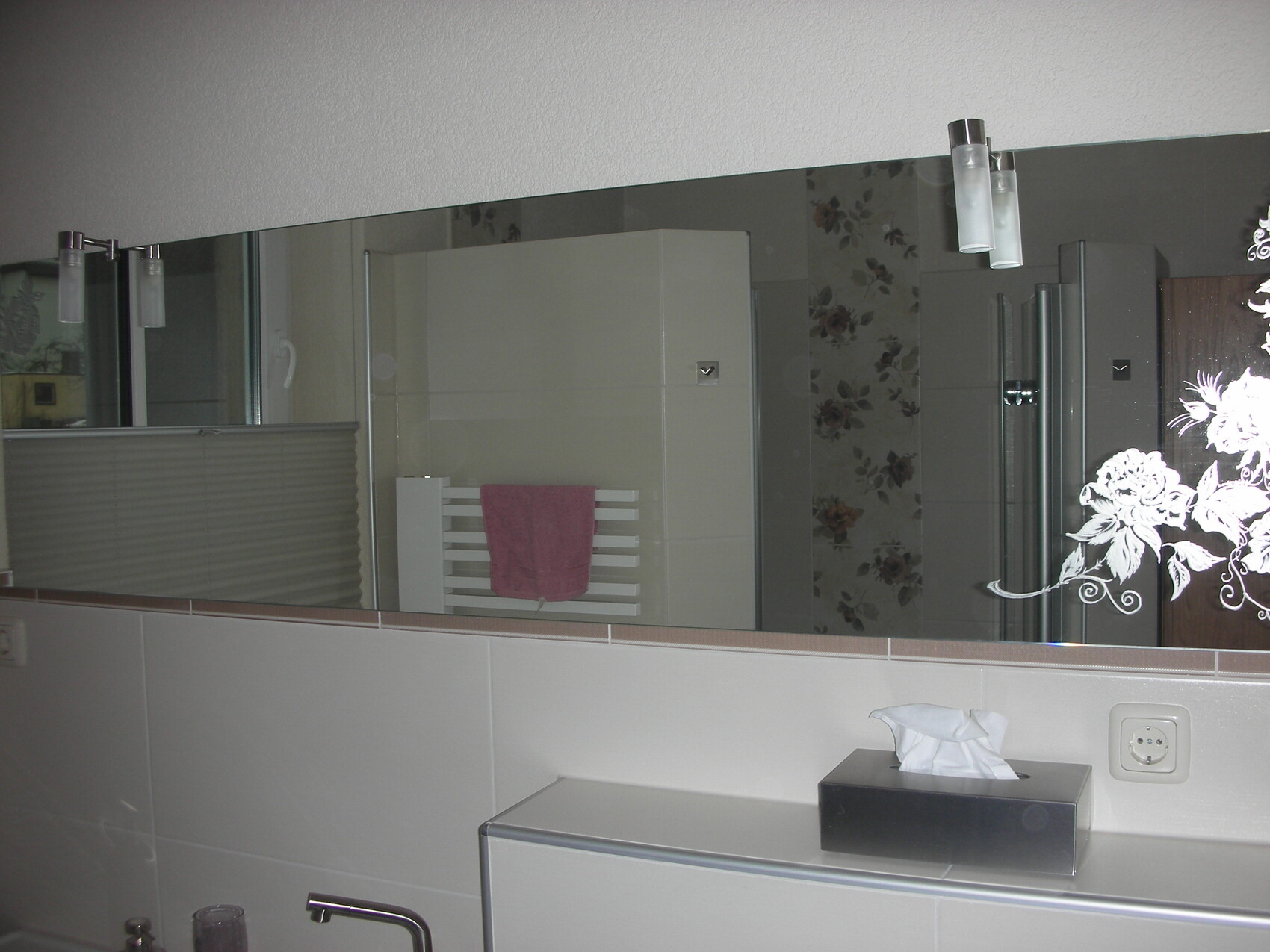 Badezimmer-Spiegel, rosa Handtuch am Heizkörper, Tissue-Box, florales Muster.