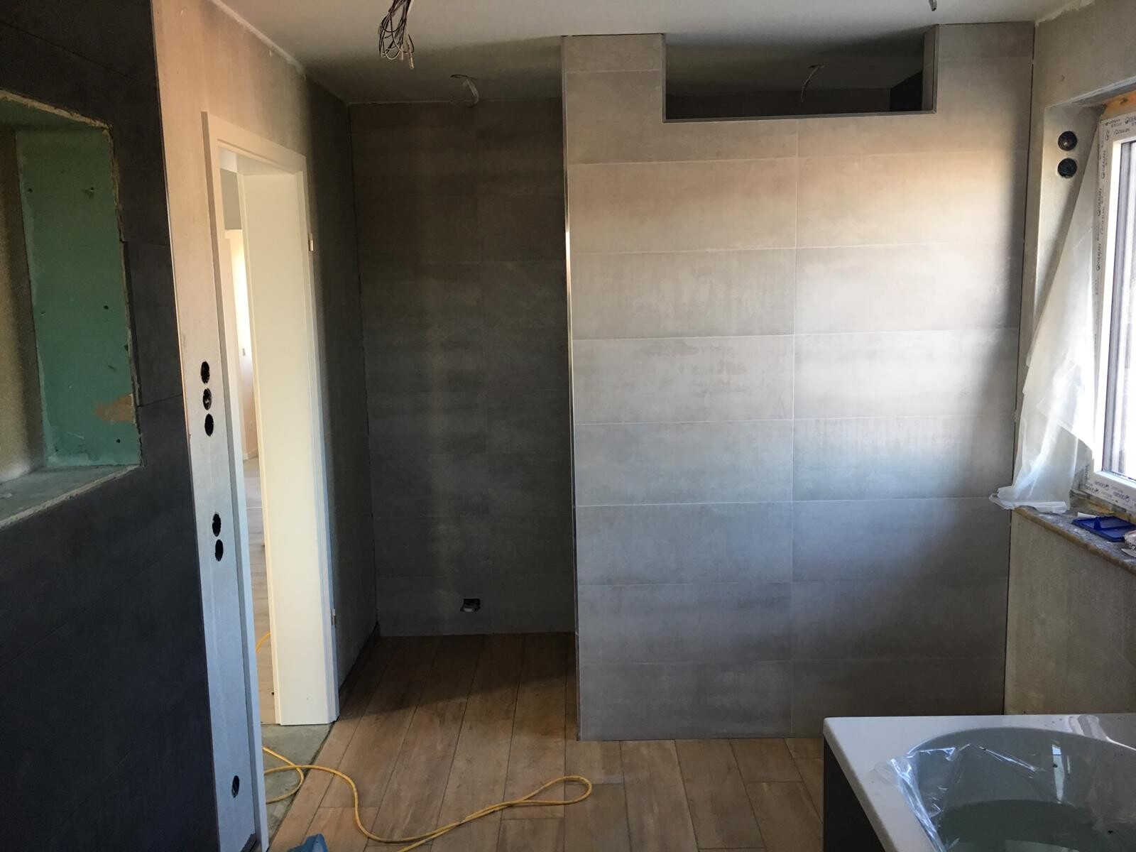 Badezimmer-Renovierung: graue Fliesenwand, Holzboden, Baukabel, Fenster mit Folie.