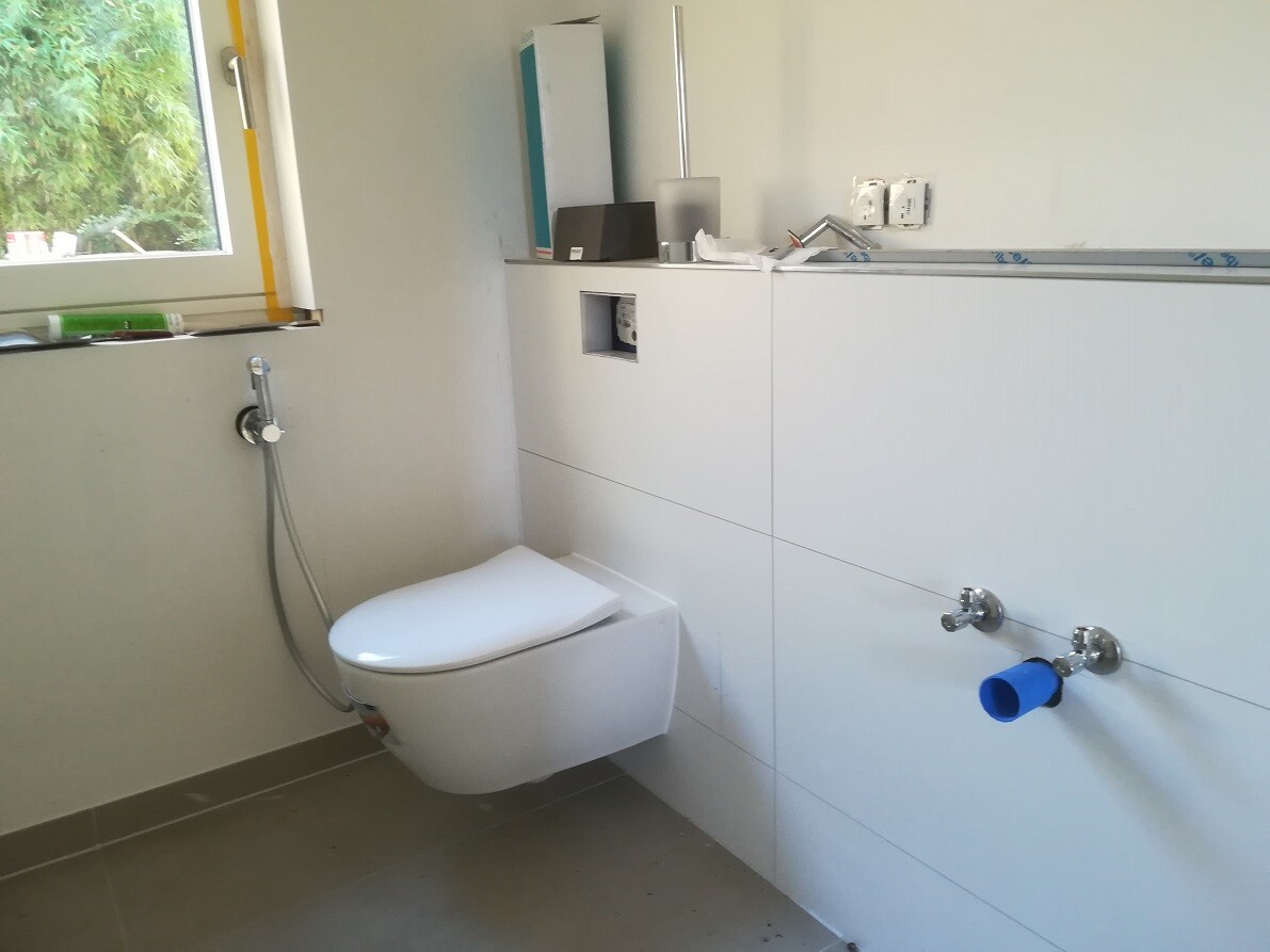 Helles Badezimmer mit wandhängendem WC und Bidetbrause sowie weißen Schränken.