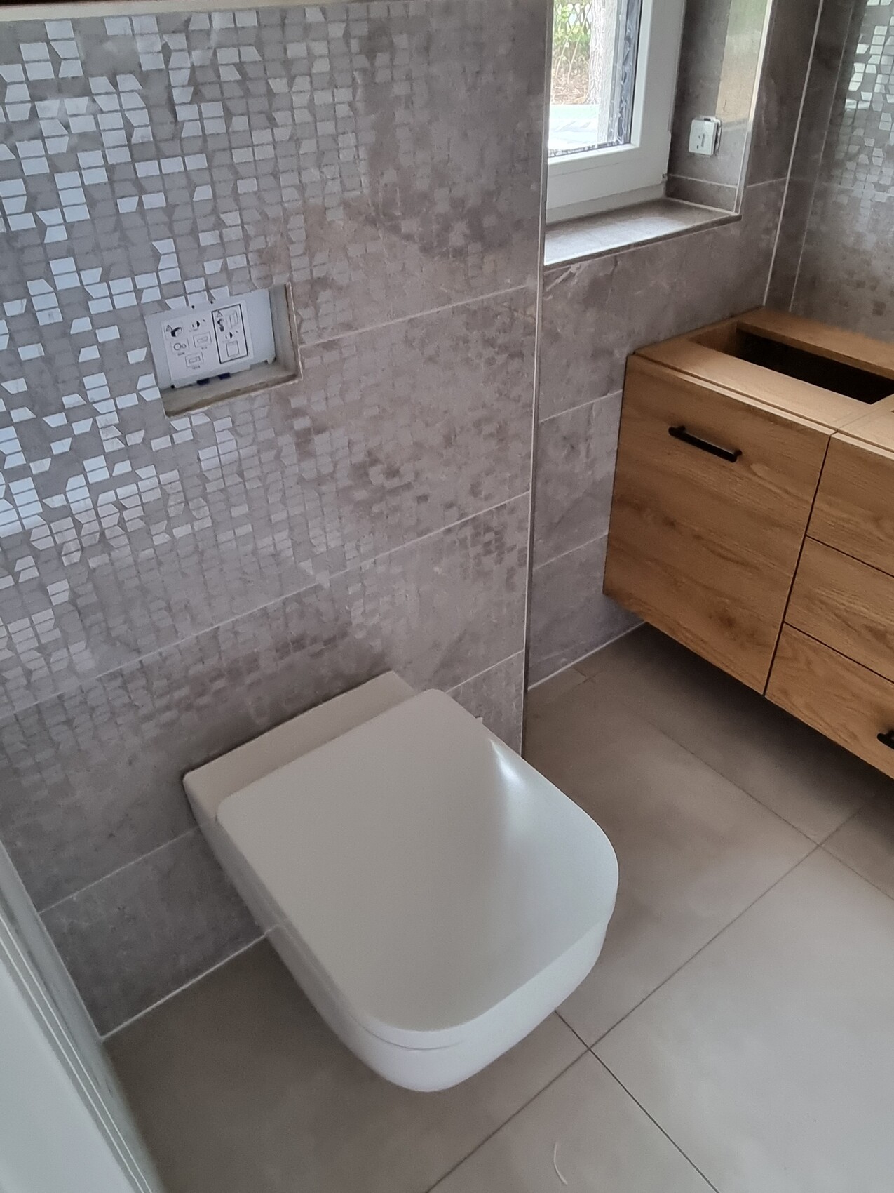 Modernes Badezimmer mit wandhängendem WC, grauen Fliesen und Holz-Waschtisch.
