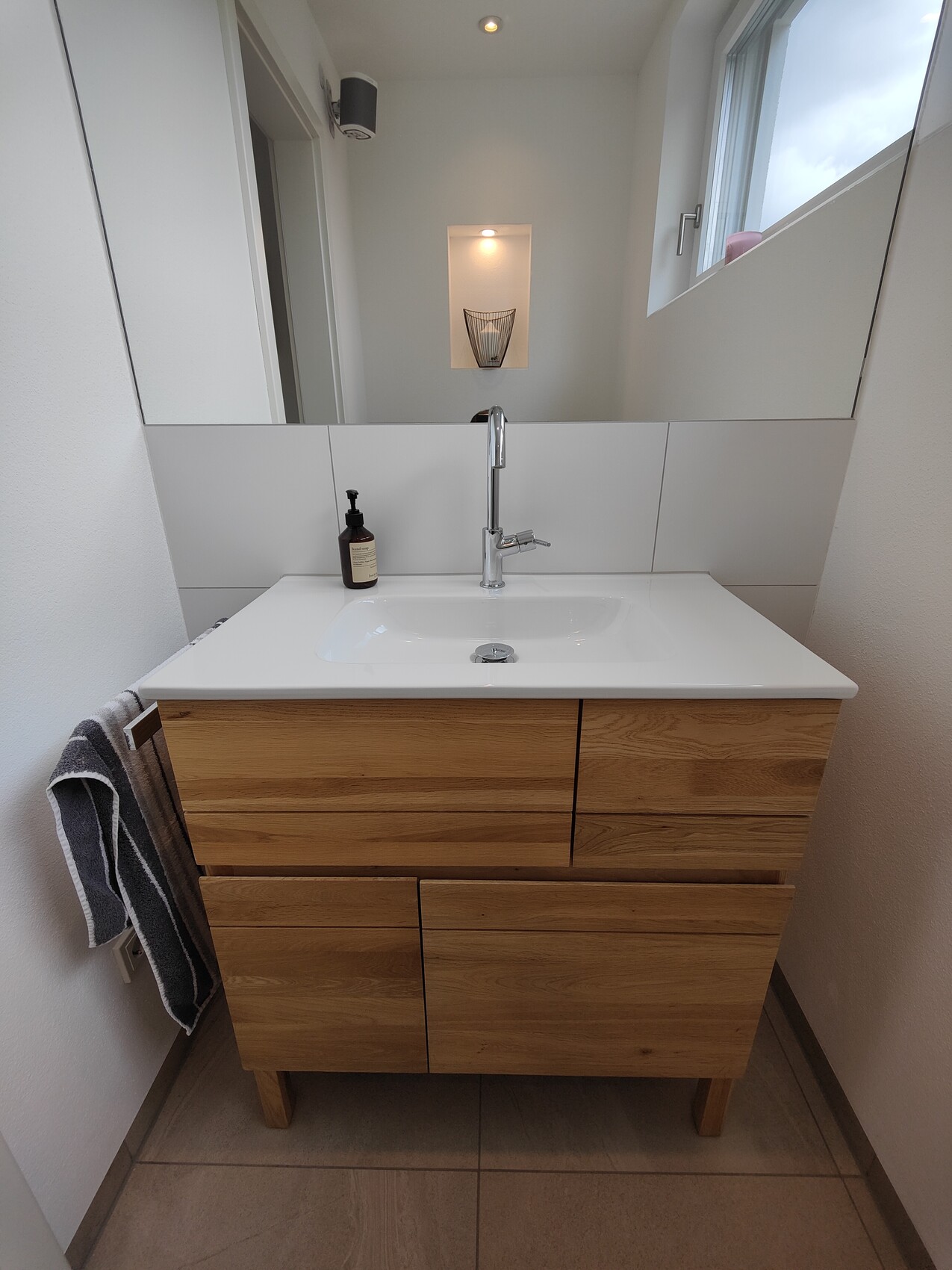 Waschbecken mit Holzunterschrank, Metallarmatur, Seifenspender und großem Spiegel.