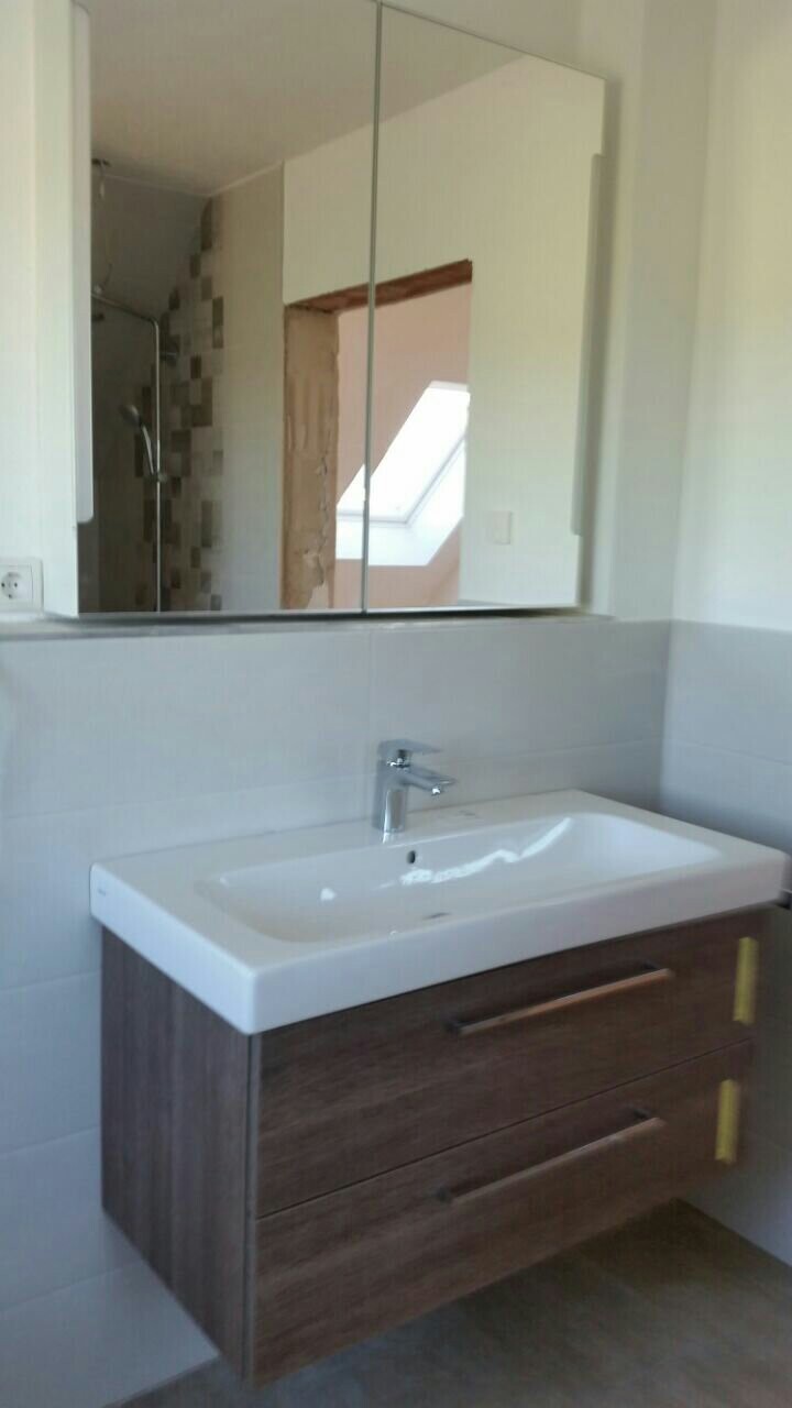 Badezimmer-Waschtisch mit Holzunterschrank, Spiegelschrank, Dusche im Hintergrund.