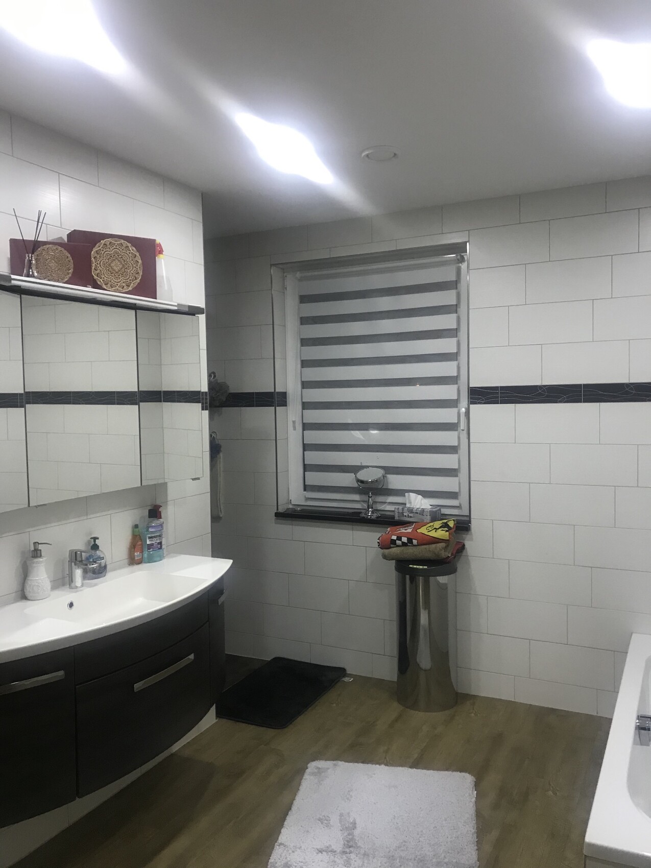 Modernes Badezimmer mit Waschbecken, Spiegel-Schrank, weißen Fliesen und Fenster mit Rollos