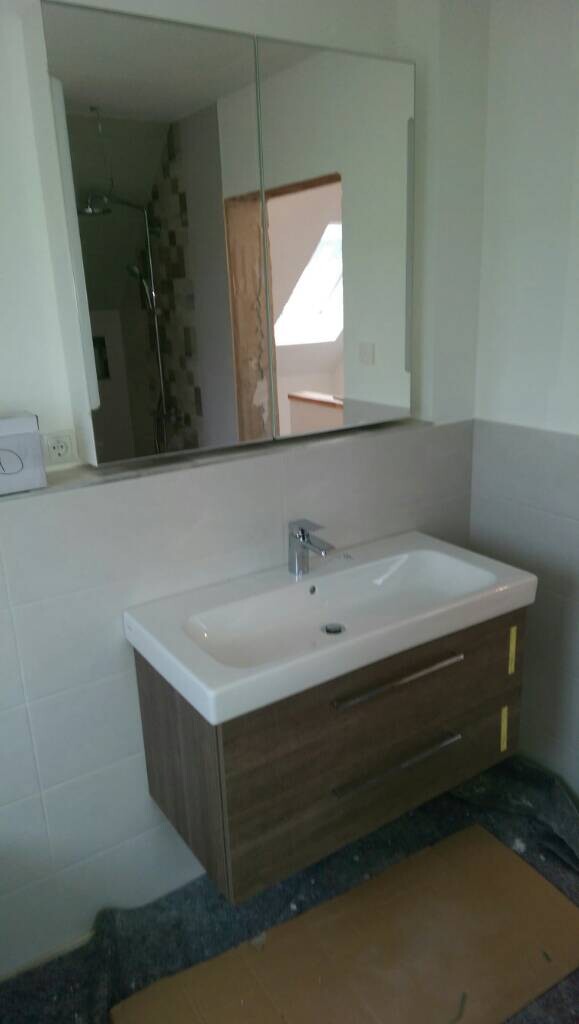 Waschbecken mit Holz-Unterschrank und Spiegelschrank, modern eingerichtetes Badezimmer; Dusche im Hintergrund.