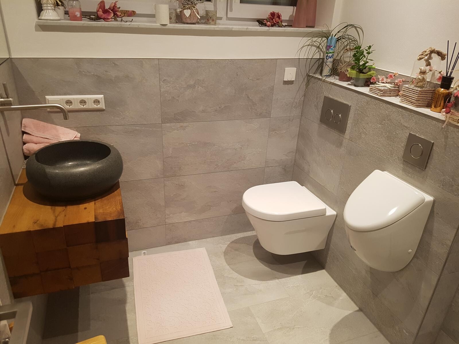 Modernes Badezimmer mit wandhängender Toilette, schwarzem Stein-Waschbecken und Holzunterbau.