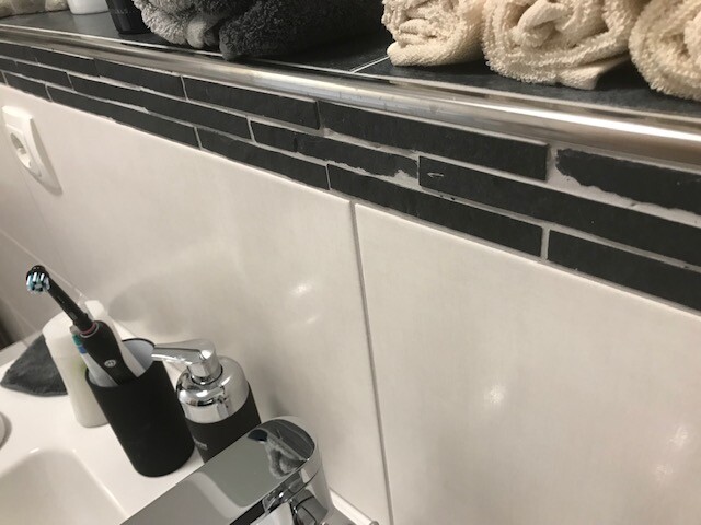 Waschtisch im Badezimmer vor schwarzer Fliesenrückwand, Seifenspender und Handtücher.
