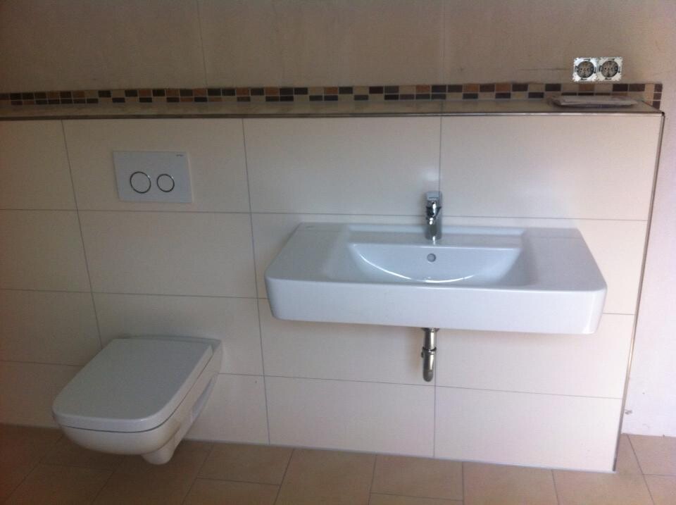 Modernes Badezimmer: Wandwaschbecken, Wand-WC und Fliesenbordüre.