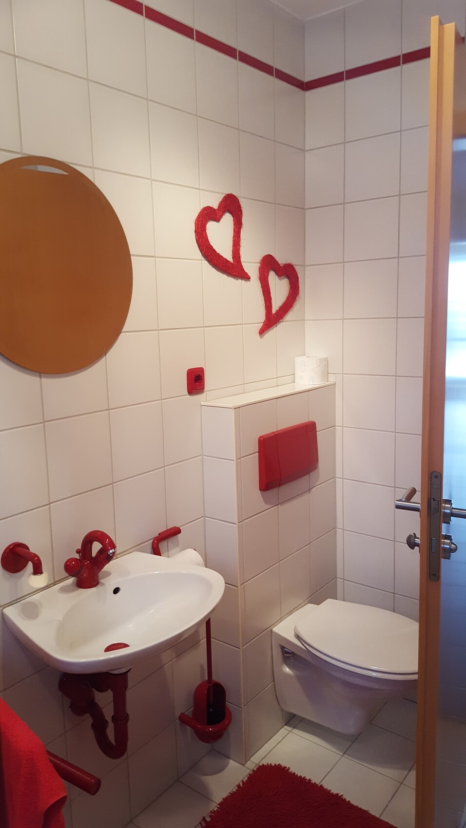 Kleines Badezimmer mit weissen Fliesen, rotem Sanitaer- und Dekoakzent
