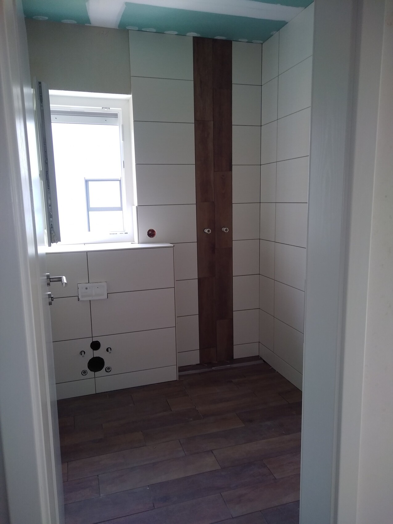 Badezimmer im Bau mit weißen Wandfliesen, dunkler Holz-Akzentleiste und Fenster