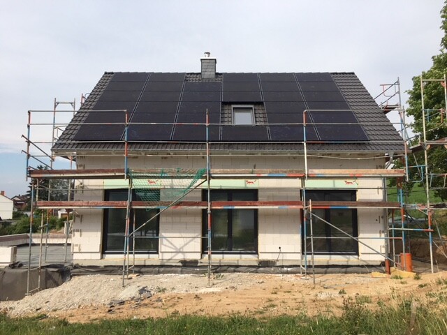 Einfamilienhaus im Bau mit Gerüst rundum und Solarpaneele auf dem Dach.