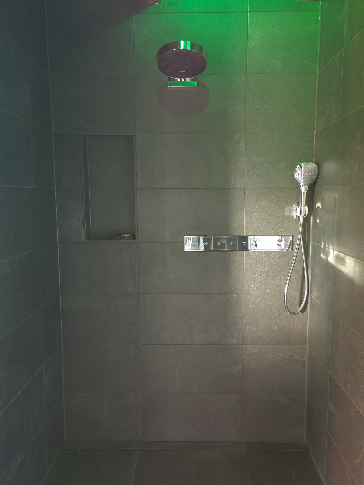 Dunkle Fliesen-Dusche mit Deckenregendusche, Handbrause rechts, Nische links.