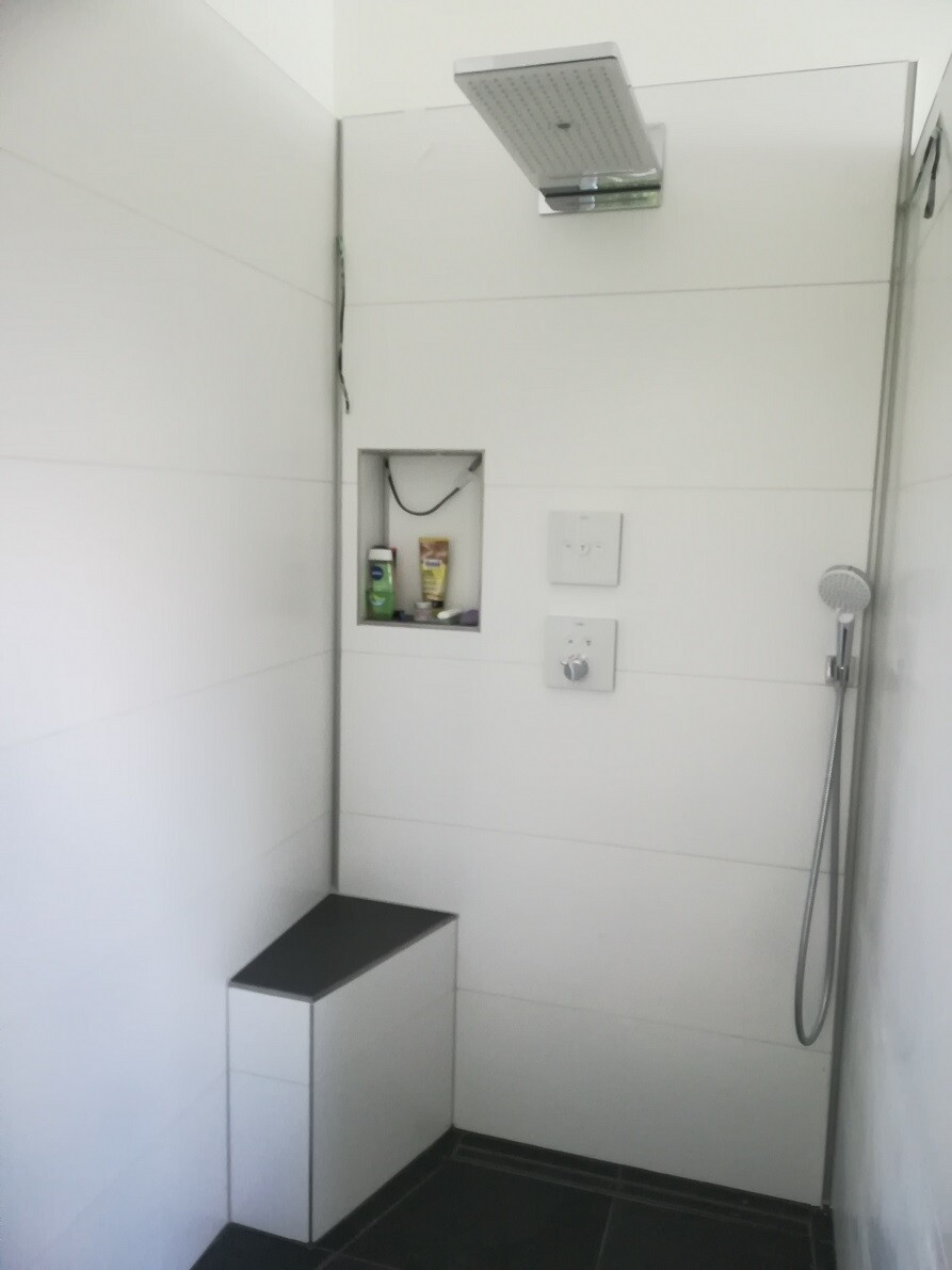 Begehbare Dusche mit Deckenregner, Handbrause, Nische mit Produkten, Sitzbank.