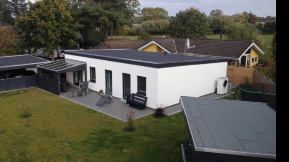 Drohnenaufnahme eines modernen, weißen Einfamilienhauses mit Terrasse und Gartenmöbeln.