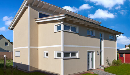 Außenansicht eines modernen beigefarbenen Einfamilienhauses mit Dachüberstand und Garten.