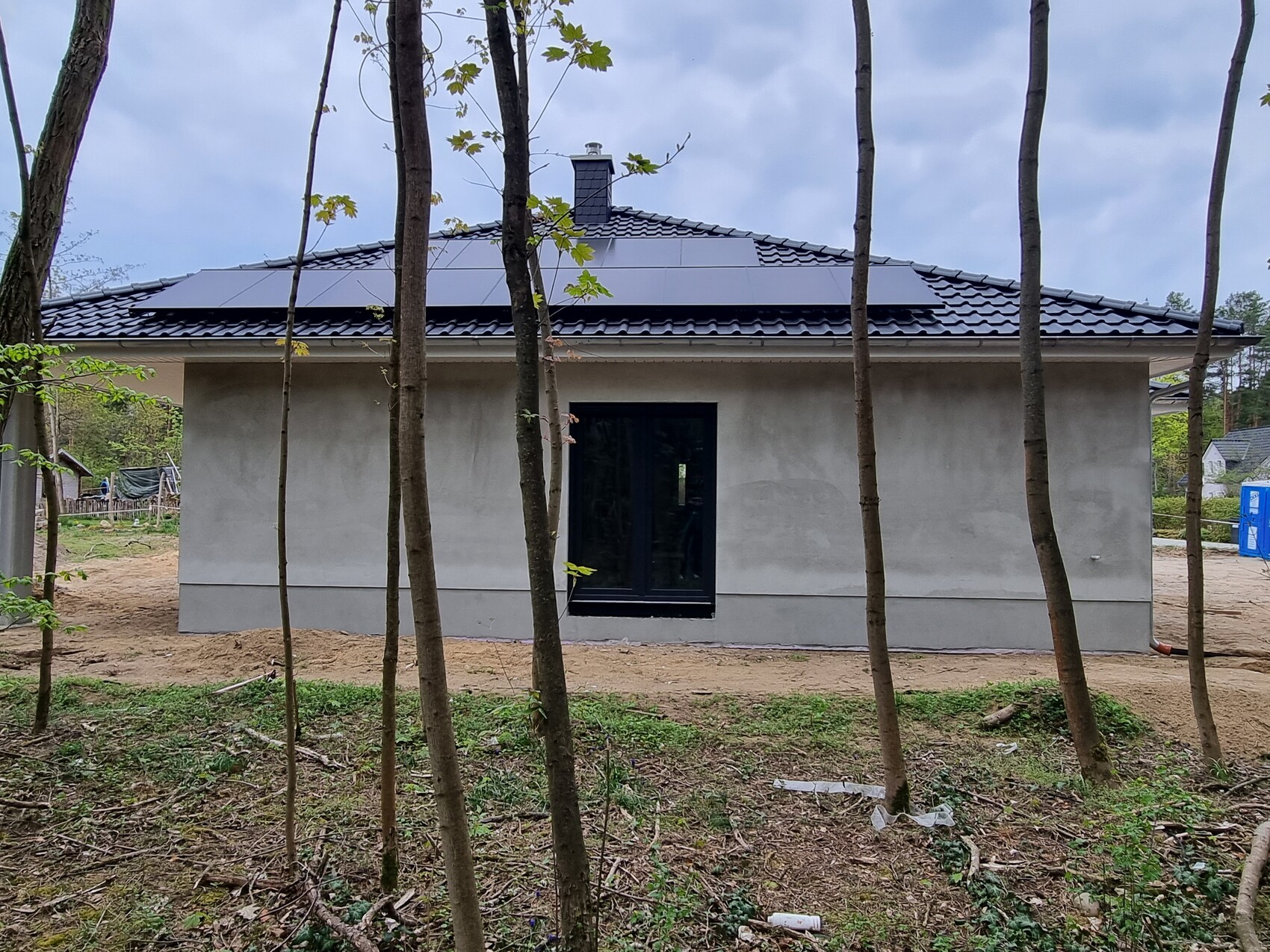Kleines Haus mit Solarmodulen auf dem Dach, von Bäumen umgeben, Baugrundstück.