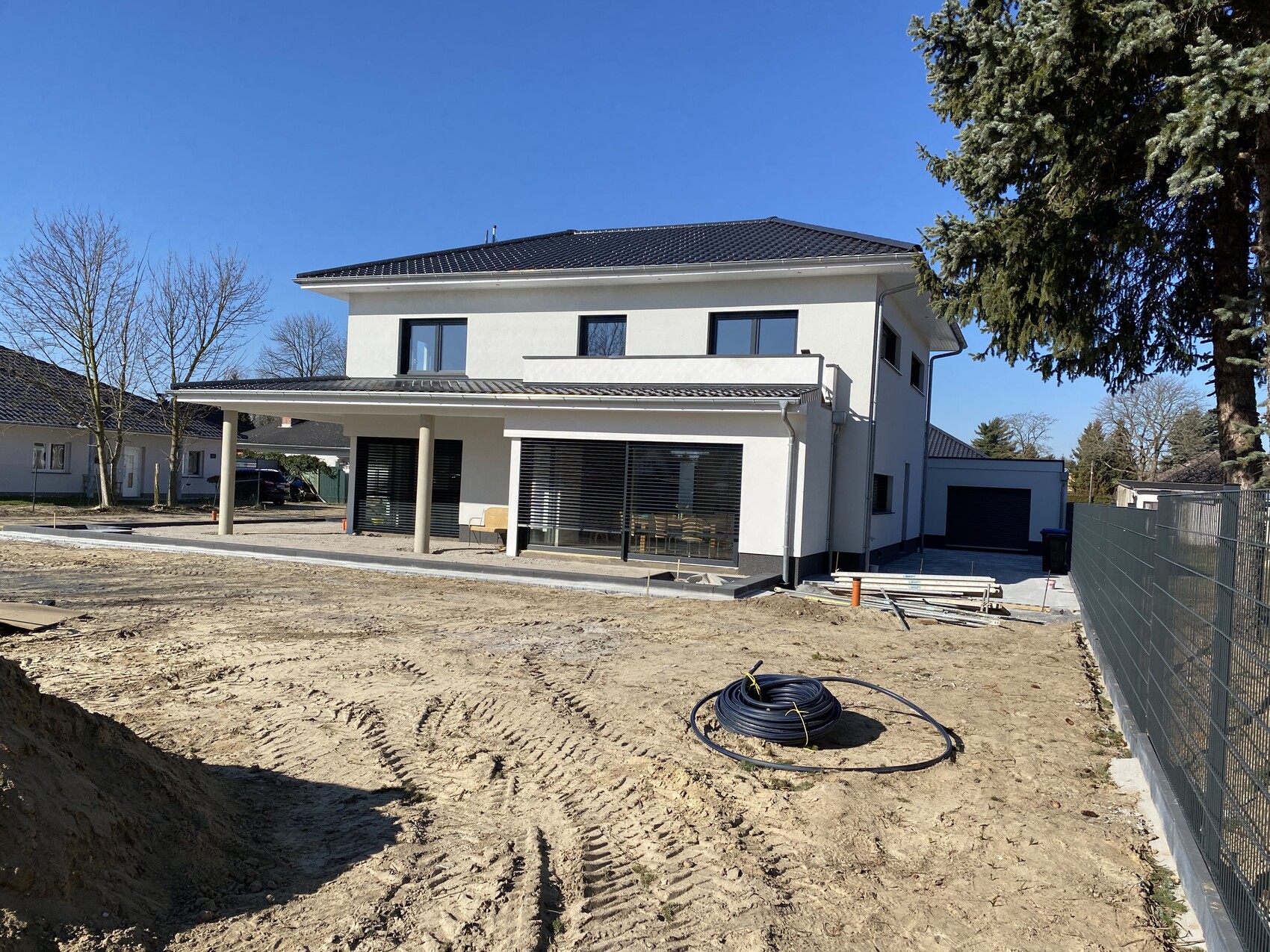 Modernes zweistöckiges Einfamilienhaus mit Terrasse; Bauplatz davor, Kabelrolle und Baumaterialien.