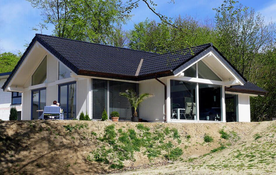 Modernes Einfamilienhaus mit großen Glasfronten und dunklem Satteldach; Person sitzt draußen