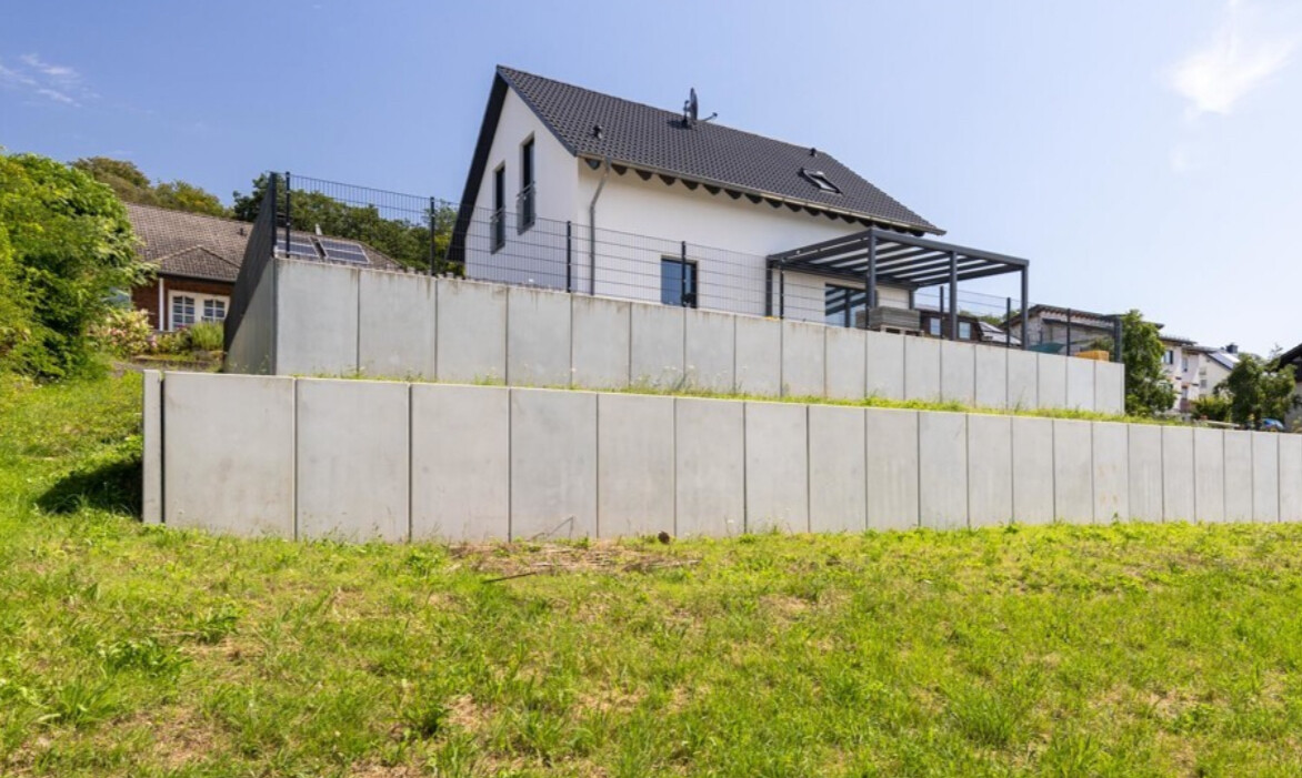 Modernes weißes Haus auf Hang, Betonmauern, Terrasse und grüne Wiese davor
