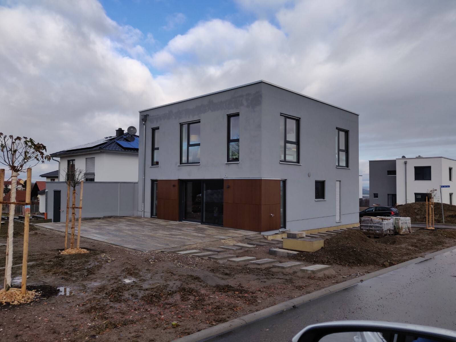 Modernes graues zweistöckiges Haus mit Terrasse, Baugelände im Vordergrund.