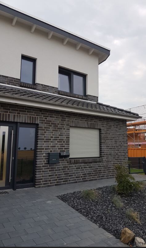Modernes zweigeschossiges Haus mit Backsteinfassade, Rollladenfenster und Kiesgarten.