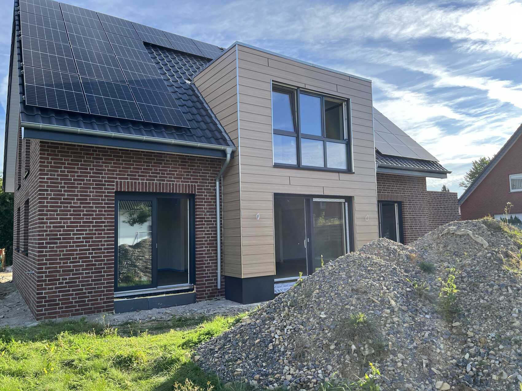 Modernes Einfamilienhaus unter Bau mit Solarpanelen, Backstein- und Holzverkleidung, Kieshügel.