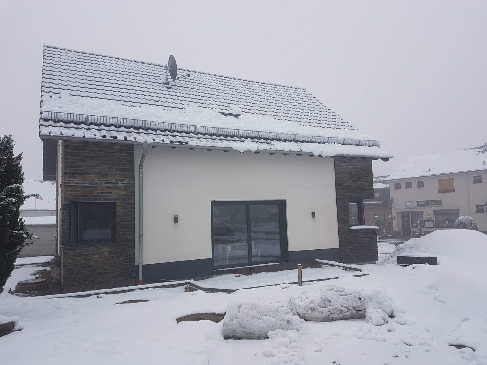 Modernes Einfamilienhaus mit Steinverkleidung, verschneitem Dach und Satellitenschüssel.