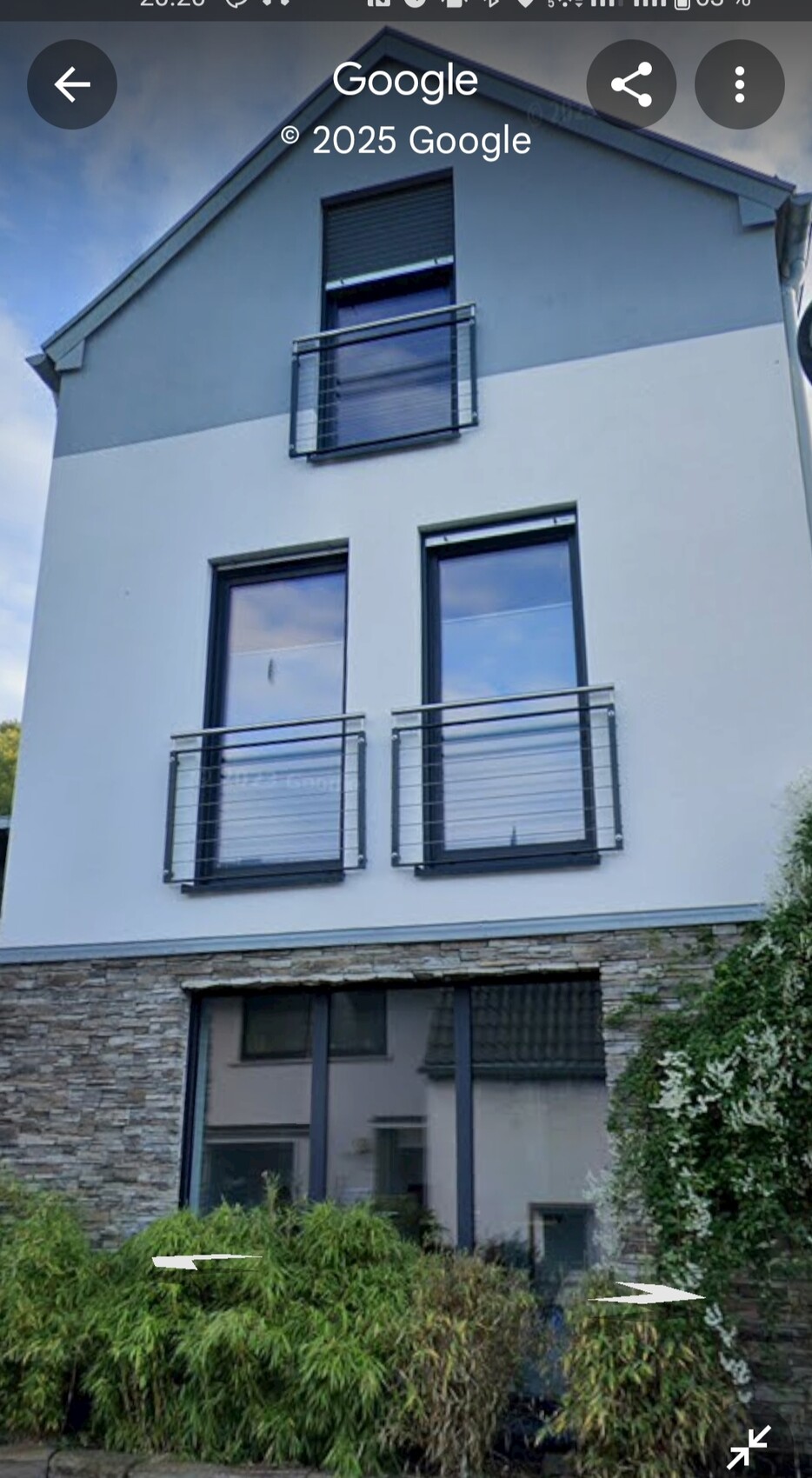 Modernes Haus mit weißen Wänden, grauer Oberseite, Balkonen und Steinverkleidung unten, Garten.