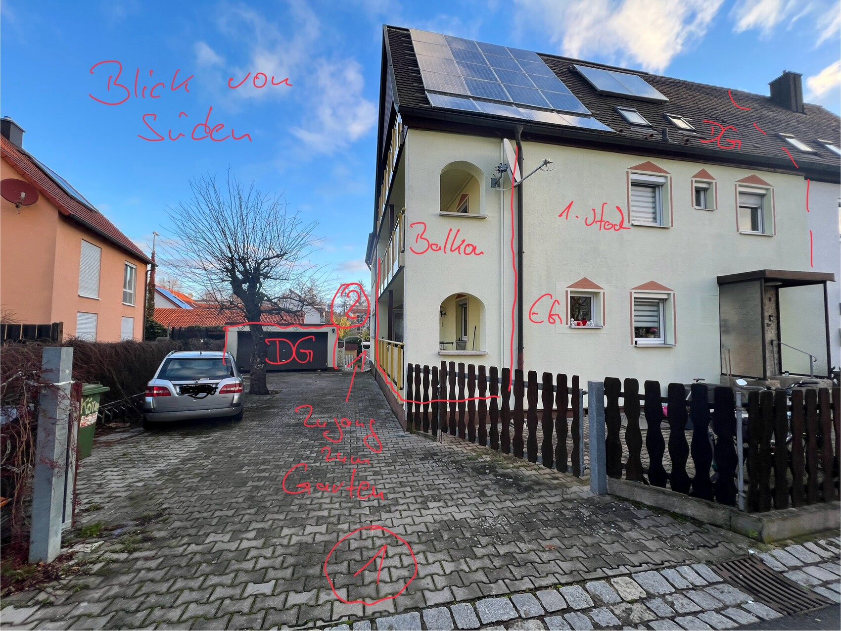 Mehrfamilienhaus mit Solaranlagen, gepflasterte Einfahrt, geparktes Auto und Gartenzaun.